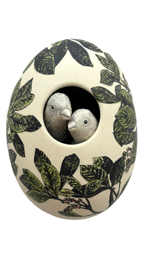 Decorative ceramic egg with leaf pattern and two small birds inside on a white background