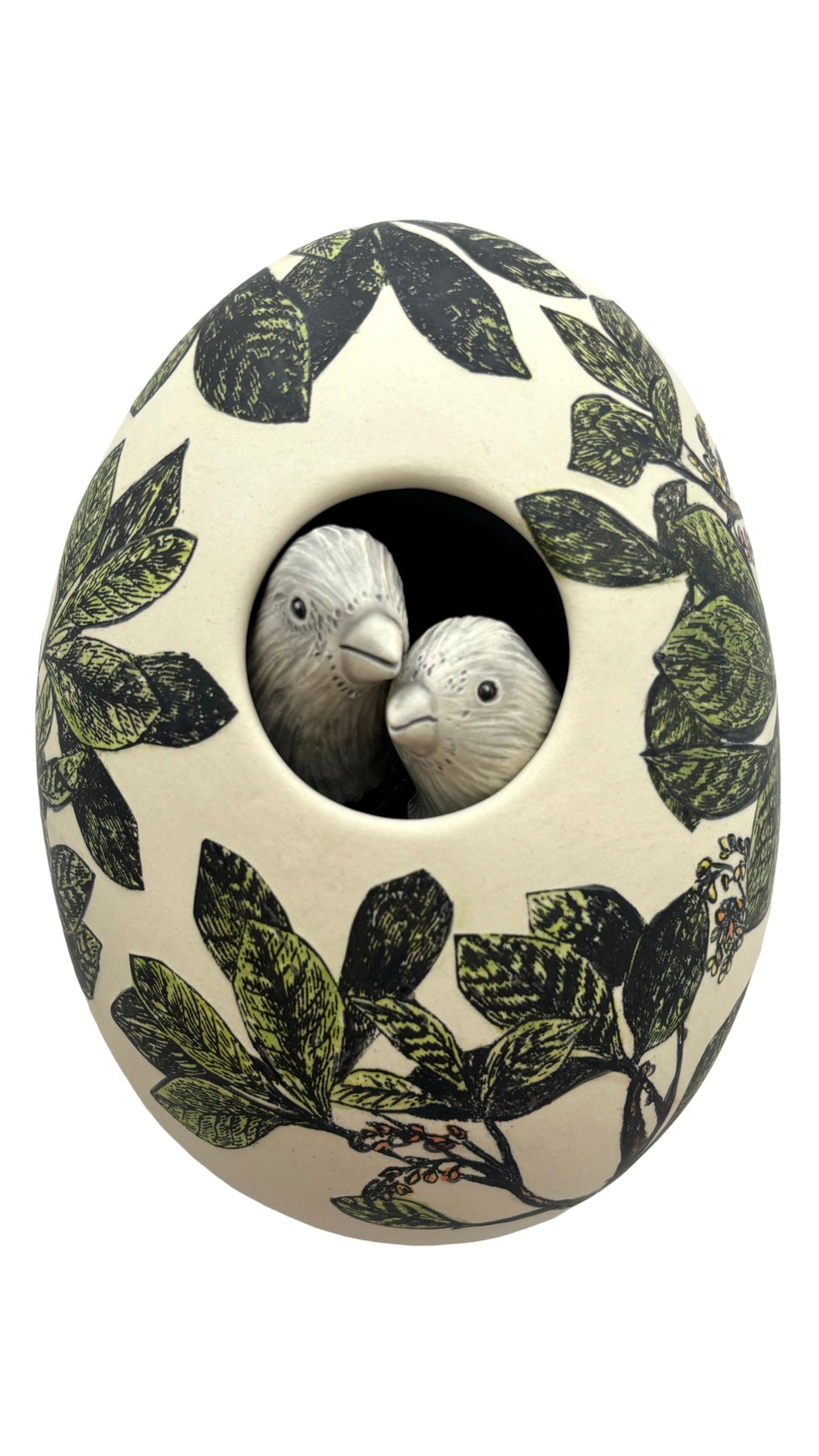 Decorative ceramic egg with leaf pattern and two small birds inside on a white background